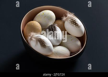 ostereier mit Federn in Schale auf schwarzem Tisch Stockfoto