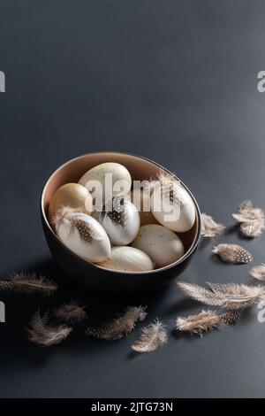 ostereier mit Federn in Schale auf schwarzem Tisch Stockfoto