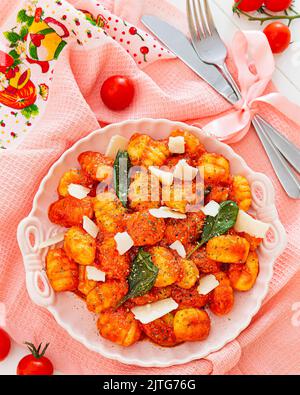 Hausgemachte Gnocchi serviert mit Tomaten, Basilikum, Parmesankäse in einem weißen antiken Teller auf einer pastellfarbenen Tischdecke mit Besteck. Gastronomie Werbung poste Stockfoto