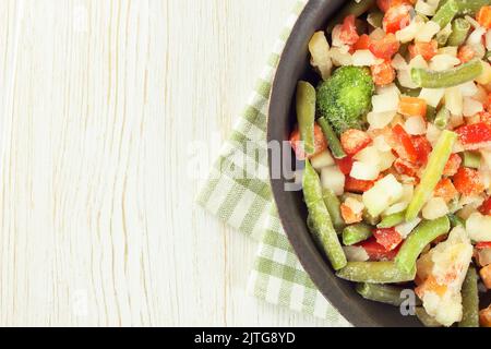 Eine Mischung aus verschiedenen gefrorenen Gemüse in schwarzer Pfanne bereit zum Kochen auf weißem Holztisch mit Platz für Text kopieren Stockfoto