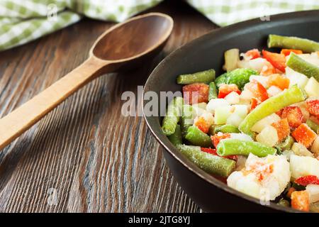 Eine Mischung aus verschiedenen gefrorenen Gemüse in schwarzer Pfanne bereit zum Kochen auf braunem Holztisch mit Platz für Text kopieren Stockfoto