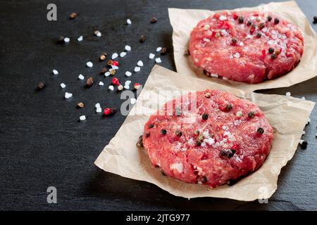 Frischer roher, hausgemachter Hackfleisch-Steak-Burger mit Gewürzen, auf einem schwarzen Schiefertisch, Platz zum Kopieren Stockfoto