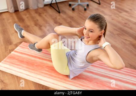 Fröhliches Teenager-Mädchen, das zu Hause auf einer Yogamatte trainiert Stockfoto