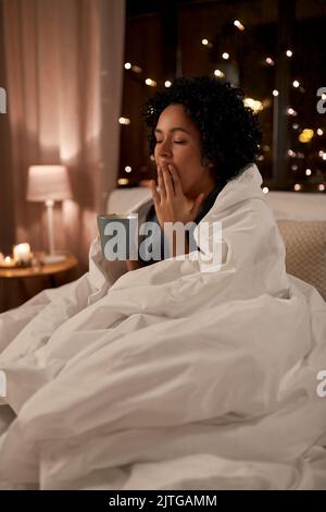 Müde Frau mit Kaffee gähnend im Bett in der Nacht Stockfoto