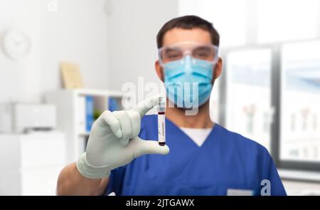 Männlicher Arzt in Maske mit Blut im Reagenzglas Stockfoto