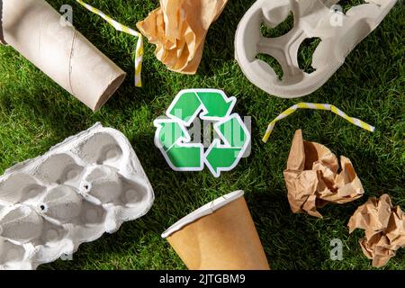 Grünes Recycling-Zeichen und Papierabfall auf Gras Stockfoto