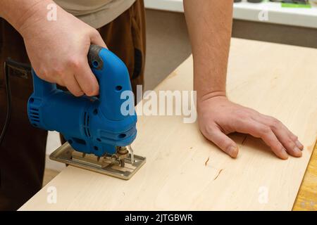 Bild von einem Mann Hand mit elektrischen Stichsäge. Nahaufnahme Prozess des Schneidens Holzbrett. Stockfoto