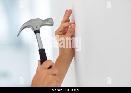 Nahaufnahme der Hände, die zu Hause Nagel an die Wand schlagen Stockfoto