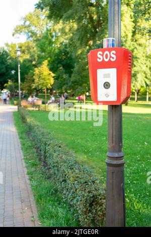 SOS, Polizei, Notruftaste im öffentlichen Park. Rote Box mit Videokamera und blauer Warnleuchte oben Stockfoto