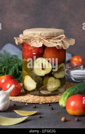 Eingelegte Gurken mit Kirschtomaten im Glas auf braunem Hintergrund mit frischen Zutaten Stockfoto