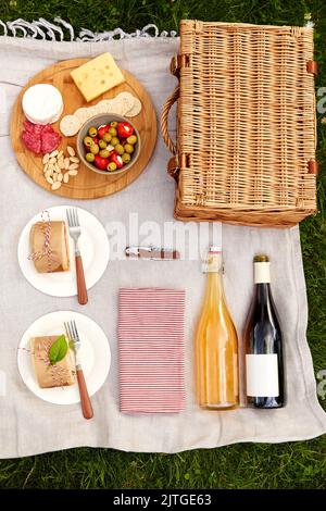 Essen, Getränke und Picknickkorb auf einer Decke auf Gras Stockfoto