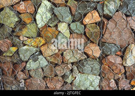 Gabion, Textur, Hintergrund. Wand aus Natursteinen und Metallzäunen. Landschaftsgestaltung. Fechten und Terrassierung Stockfoto