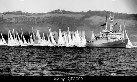 AJAXNETPHOTO. 1988. PLYMOUTH, ENGLAND. - RUNDENRENNEN IN GROSSBRITANNIEN - EINHÜLLEN-WETTKÄMPFER STARTEN IN PLYMOUTH ZU EINEM FLIEGENDEN START, WÄHREND SIE SICH AUFMACHEN, UM DIE STARTLINIE ZU ÜBERQUEREN, DIE MIT DEM PFEIL DER GUARDSHIP-FREGATTE-HMS MARKIERT IST. FOTO: JONATHAN EASTLAND/AJAX REF:340 222904 65 Stockfoto