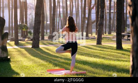 Eine schöne junge Frau, die in einem Park Yoga praktiziert Stockfoto