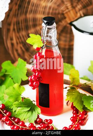 Gesunder hausgemachter roter Johannisbeersirup in einer Glasflasche für kalte Sommergetränke. Rustikaler Stil. Konzept für alkoholfreie Getränke. Selektiver Fokus. Stockfoto