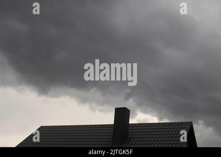 Defokussieren Sie das Stahldach auf dem Hintergrund des dunklen Himmels. Dunkle Regenwolken über dem modernen Dach. Dach mit neuen schwarzen Dachziegeln doppelte Klappe auf Wohn-ordnungsgemäße Stockfoto