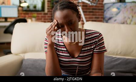 Weibliche Mitarbeiterin mit Kopfschmerzen, die von zu Hause aus arbeitet, sich gestresst und überfordert vor dem Laptop fühlt. Müde frustrierte Frau, die an Migräne und Anspannung leidet, Fernarbeit. Stockfoto