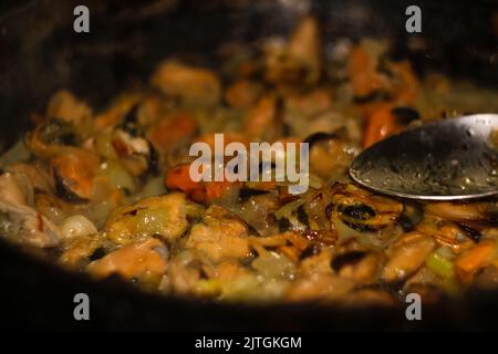 Muscheln auf der Pfanne defokussieren. Köstliche Meeresfrüchte-Muscheln mit Papagei und Zwiebeln. Haufen geschälter Muscheln mit Löffel Nahaufnahme auf dunklem Hintergrund. Delicio Stockfoto