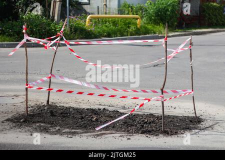 Unschärfe-Reparatur-Straße. Schutz durch rotes und weißes Schutzband. Straßenreparaturschild. Warnschilder für Straßenarbeiten am Straßenrand. Sanierung der Straße. Frischer Asphalt. Stockfoto