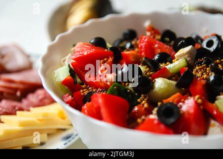 Sommersalat mit Nahaufnahme defokussieren. Klassischer griechischer Salat aus Tomaten, Gurken, rotem Pfeffer, Zwiebeln mit Oliven, Orangen und Feta. Frisches gemischtes Gemüse Stockfoto