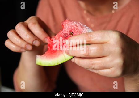 Unschärfe Frau essen Wassermelone. Die Hand der Frau hält ein Stück Wassermelone zu Hause. Nahaufnahme weiblicher Hände mit roten Früchten. Nicht fokussiert. Stockfoto