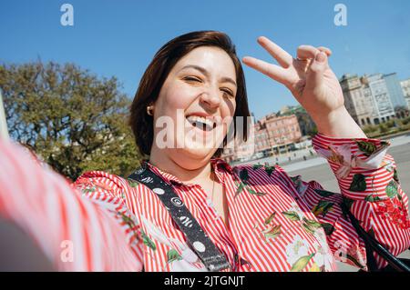 Selfie-Portrait des Inhalts lateinische kaukasische argentinierin plus size junge Frau mit kurzen Haaren und lächelnd im Freien stehend und Frieden und Liebe Zeichen tun Stockfoto