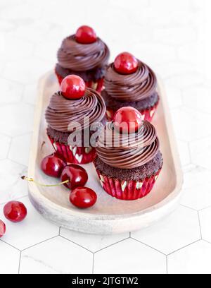 Cupcakes aus dunkler Schokolade mit Kirschen und Schokoladenganache Stockfoto