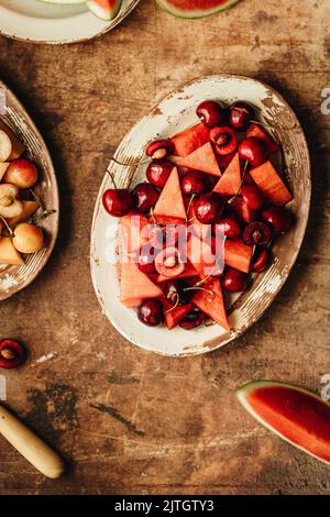 Ein frischer Obstsalat aus Kirschen und Wassermelone auf einem rustikalen Teller Stockfoto