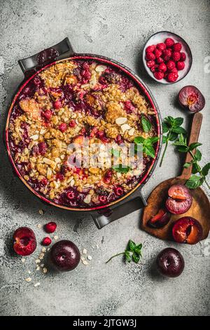 In einer runden Backform mit Pflaume und Himbeeren auf der Seite bröseln Stockfoto