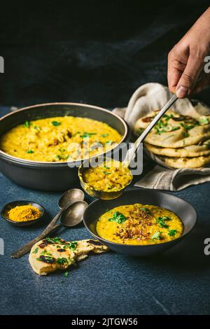 Gelbe Linsen in einer großen Schüssel mit Curry in einer Servierschüssel mit Naan-Brot Stockfoto