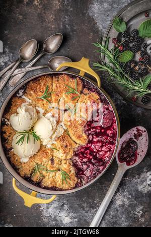 Beerenkrümel oder Kuchen im niederländischen Ofen mit Knödelspitze und ungekochten Beeren auf der Seite Stockfoto