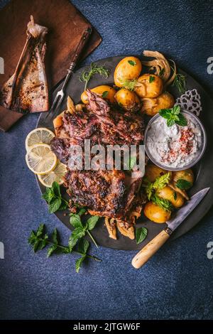 Geschreddertes Lamm mit ganzen gekochten Kartoffeln und Joghurt-Dip auf der Seite, dunkler Hintergrund Stockfoto