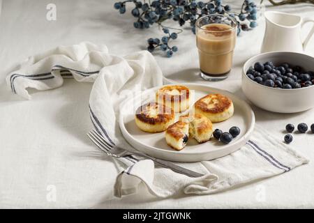 Syrniki mit Heidelbeeren und Kaffee. Leckeres Frühstück. Gebratene Quark (Quark) Pfannkuchen; Stockfoto