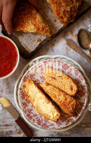 Ein herzhafter Scone mit Käse in Scheiben und Butter und Speck sowie eine Tasse Suppe Stockfoto