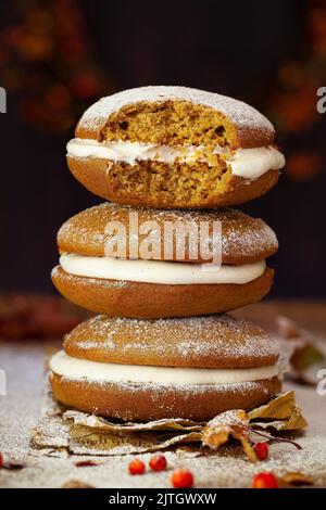 Drei Kürbis-Whoopie-Pasteten, gefüllt mit Buttercreme. Sie sind aufeinander gestapelt und man hat einen Bissen daraus genommen. Stockfoto