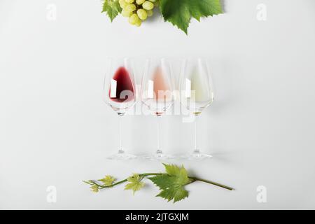 Flaches Lay von Rot-, Rosen- und Weißwein in Gläsern und Rebenblätter auf weißem Hintergrund. Weinbar, Weingut, Weinverkostung Konzept. Minimalisti Stockfoto
