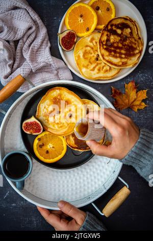 Lmond-Milch-Pfannkuchen mit Orangenscheiben, Feigen und Schokoladenstückchen auf zwei Keramikplatten, einer davon in einem weißen runden Tablett und begleitet von Stockfoto