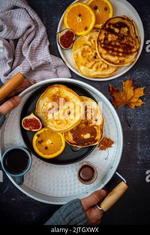 Mandelmilchpfannkuchen, serviert mit Orangenscheiben, Feigen und Schokoladenstückchen auf zwei Keramikplatten, einer davon in einem weißen runden Tablett und begleitet b Stockfoto