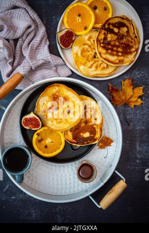 Mandelmilchpfannkuchen, serviert mit Orangenscheiben, Feigen und Schokoladenstückchen auf zwei Keramikplatten, einer davon in einem weißen runden Tablett und begleitet b Stockfoto