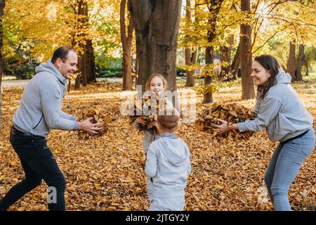 Familie mit Haufen von Ahornblättern Spaß im Wald werfen Blätter ineinander. Konzept Herbst, gelbe Blätter, Herbststimmung. Frohe Familie Stockfoto
