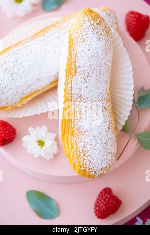 Eclairs Kuchen.Eclair Kuchen und Himbeeren auf einem rosa Podium auf einem fuchsia Hintergrund.Choux Gebäck. Stockfoto