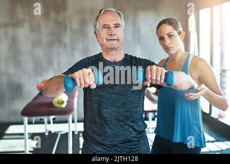 Fit bleiben in jeder Phase des Lebens. Ein älterer Mann mit Gewichten mit Hilfe eines Physiotherapeuten. Stockfoto