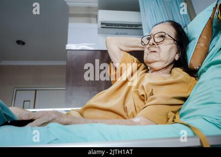 Kranke südostasiatische weibliche ältere Patientin, die sich während der medizinischen Behandlung im Krankenhaus im Bett entspannt Stockfoto