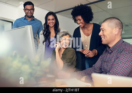 Positive Spieler sorgen für ein erfolgreiches Team. Eine Gruppe von Geschäftsleuten diskutiert etwas auf einem Computer in einem Büro. Stockfoto