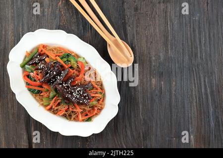 Japchae, Glasnudeln mit Gemüse und Rindfleisch, serviert auf weißem Teller. Authentische koreanische Küche, Ansicht von oben mit Kopierbereich Stockfoto