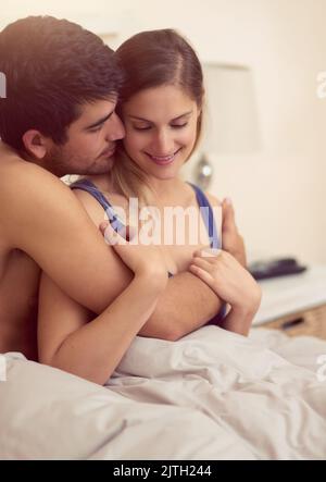 Halte mich nah an deinem Herzen. Ein liebevolles junges Paar, das sich im Bett eine intime Umarmung teilt. Stockfoto