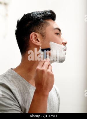 Ein junger Mann, der sich zu Hause den Bart rasiert, ist krank und hat ein glattes Gesicht. Stockfoto