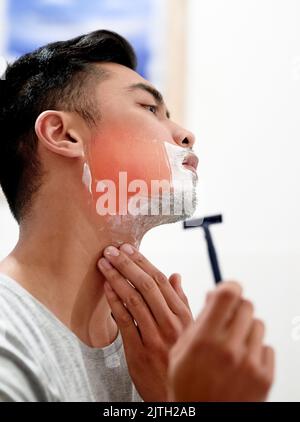 Ein junger Mann zu Hause bekommt von der Rasur mit einem Einwegrasierer einen Rasierbrand im Gesicht. Stockfoto