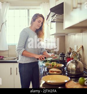 Vorbereitung einer gesunden und ausgewogenen Mahlzeit. Eine attraktive junge Frau bereitet zu Hause eine nahrhafte Mahlzeit zu. Stockfoto