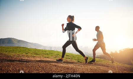 Entdecken Sie, wie weit Sie sich treiben können. Ein sportliches Paar auf einer Bergstraße. Stockfoto